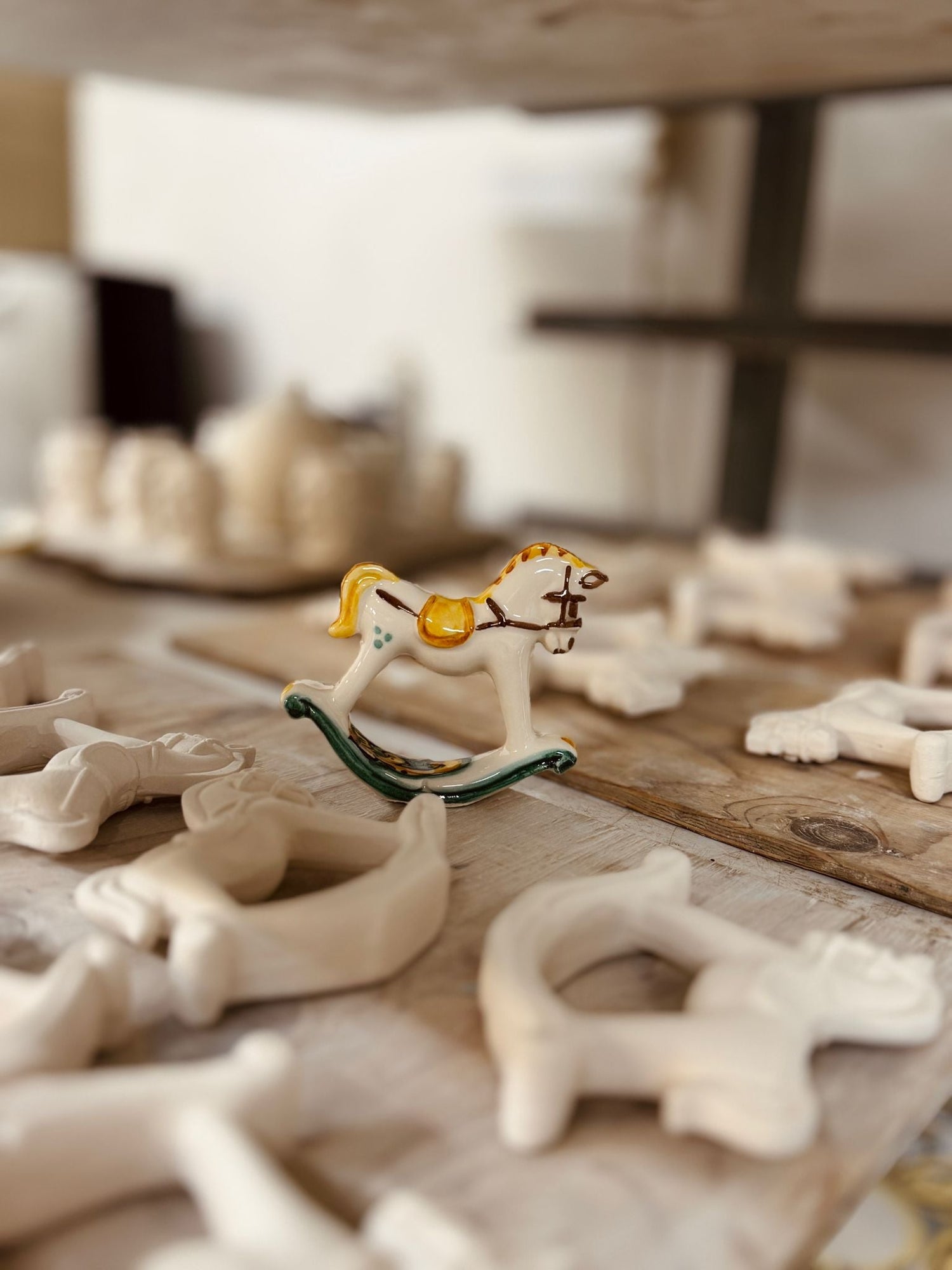 Small handcrafted Sicilian ceramic rocking horse surrounded by unfinished artisan clay pieces inside a traditional pottery workshop.