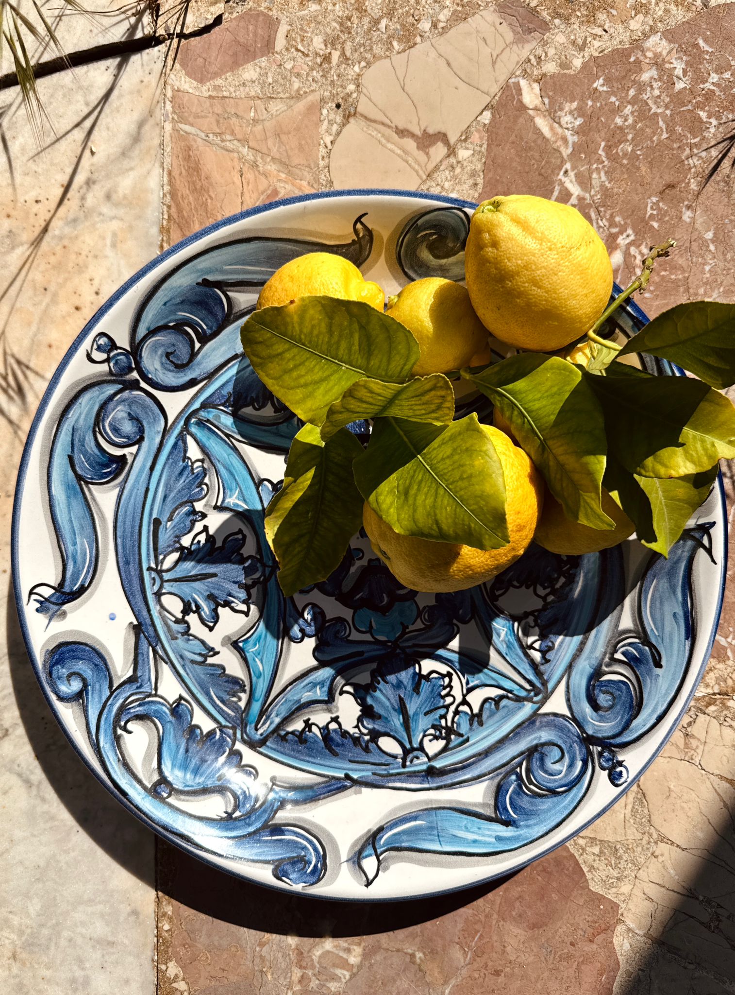 Decorative ceramic plate with blue and white patterns holding lemons on a stone surface.