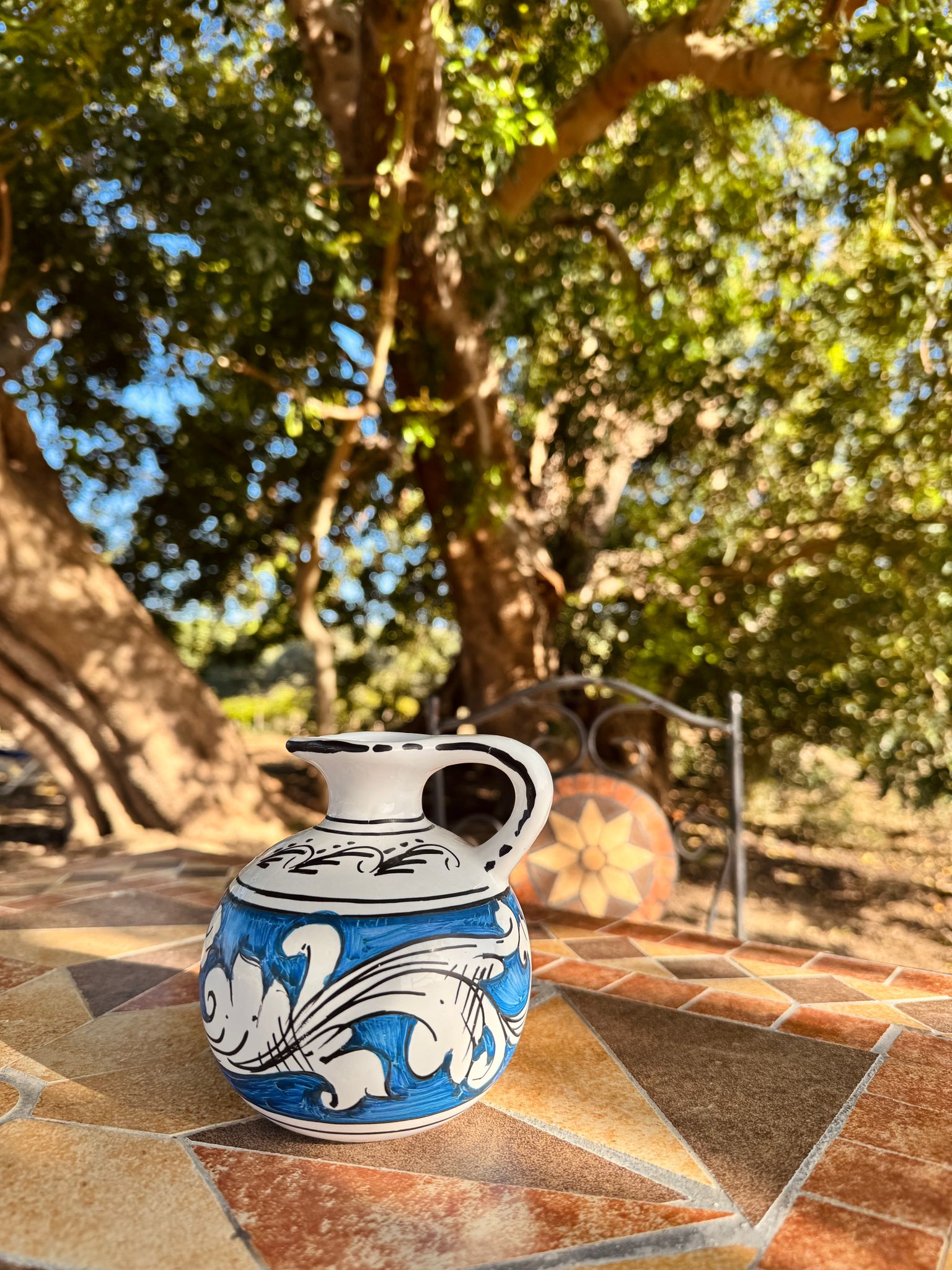 Ceramic pitcher with blue and white design on a stone surface with trees in the background