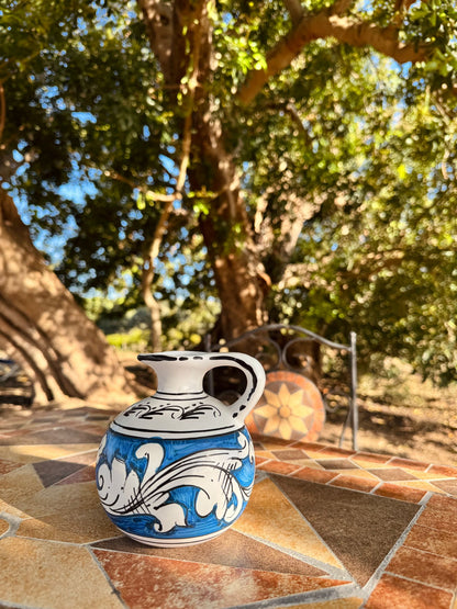 Ceramic pitcher with blue and white design on a stone surface with trees in the background