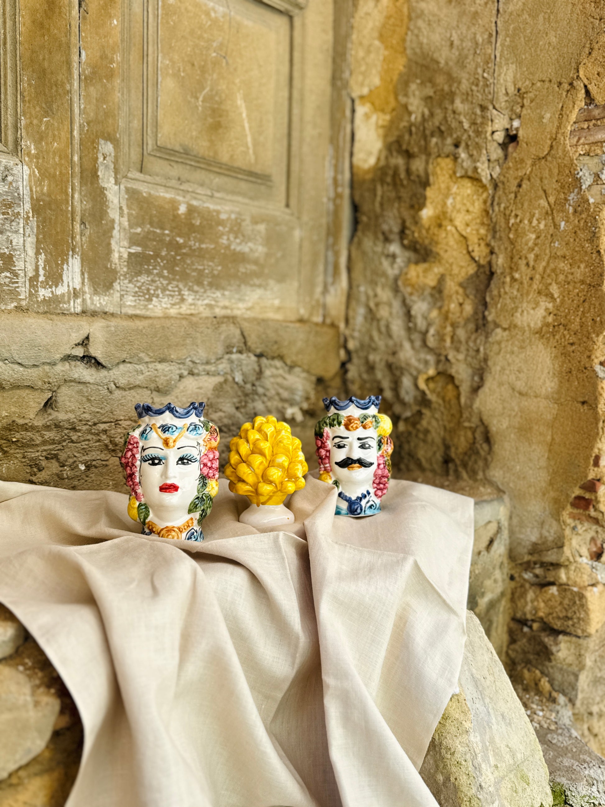 Decorative ceramic pieces on a tablecloth against an old stone wall.