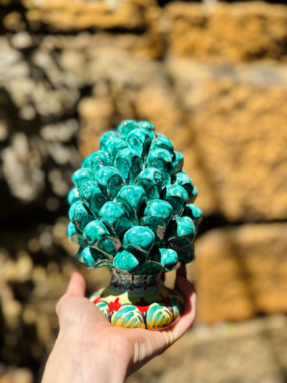 Hand holding a decorative green pine cone against a blurred natural background