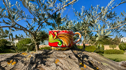 Decorative ceramic cup with a colorful design on a tree stump with an olive tree in the background.