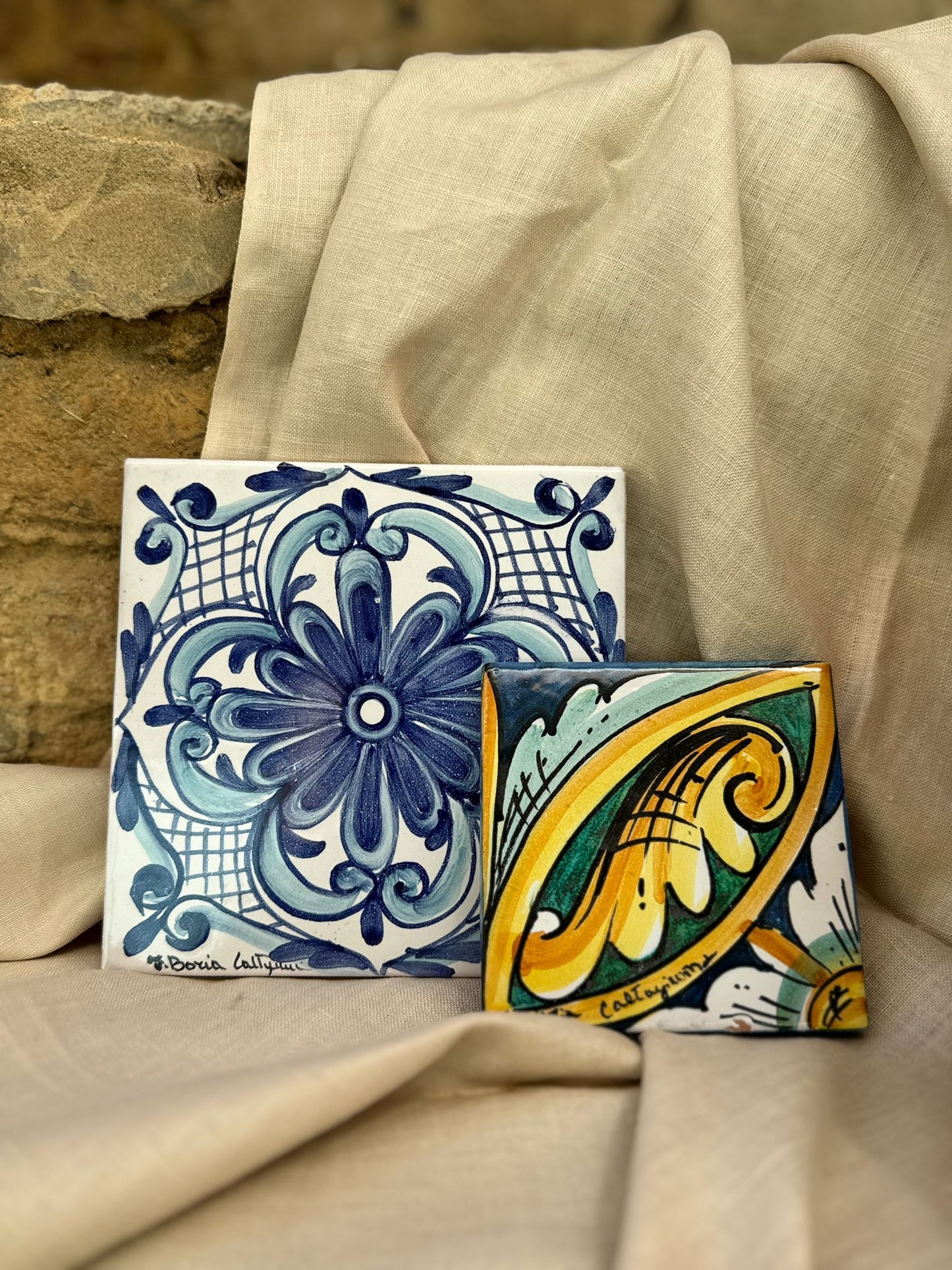 Two decorative tiles with intricate patterns on a beige fabric background