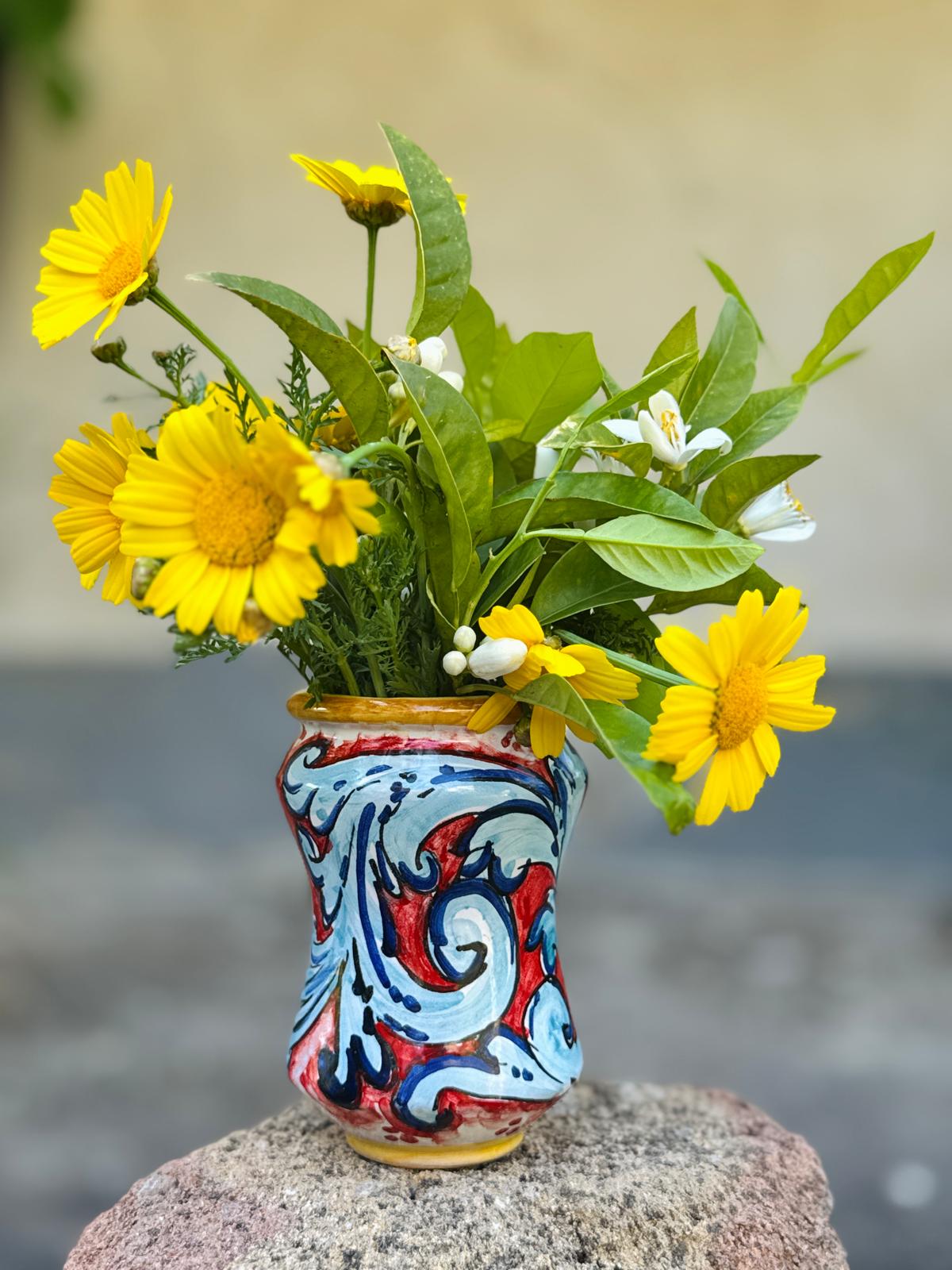 Decorative vase with colorful patterns containing a bouquet of yellow and green flowers on a blurred background
