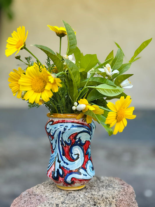Decorative vase with colorful patterns containing a bouquet of yellow and green flowers on a blurred background