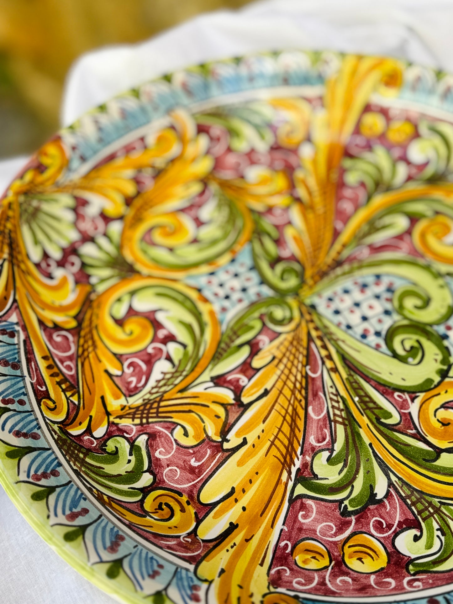 Decorative ceramic plate with intricate patterns in yellow, green, and red on a white background.