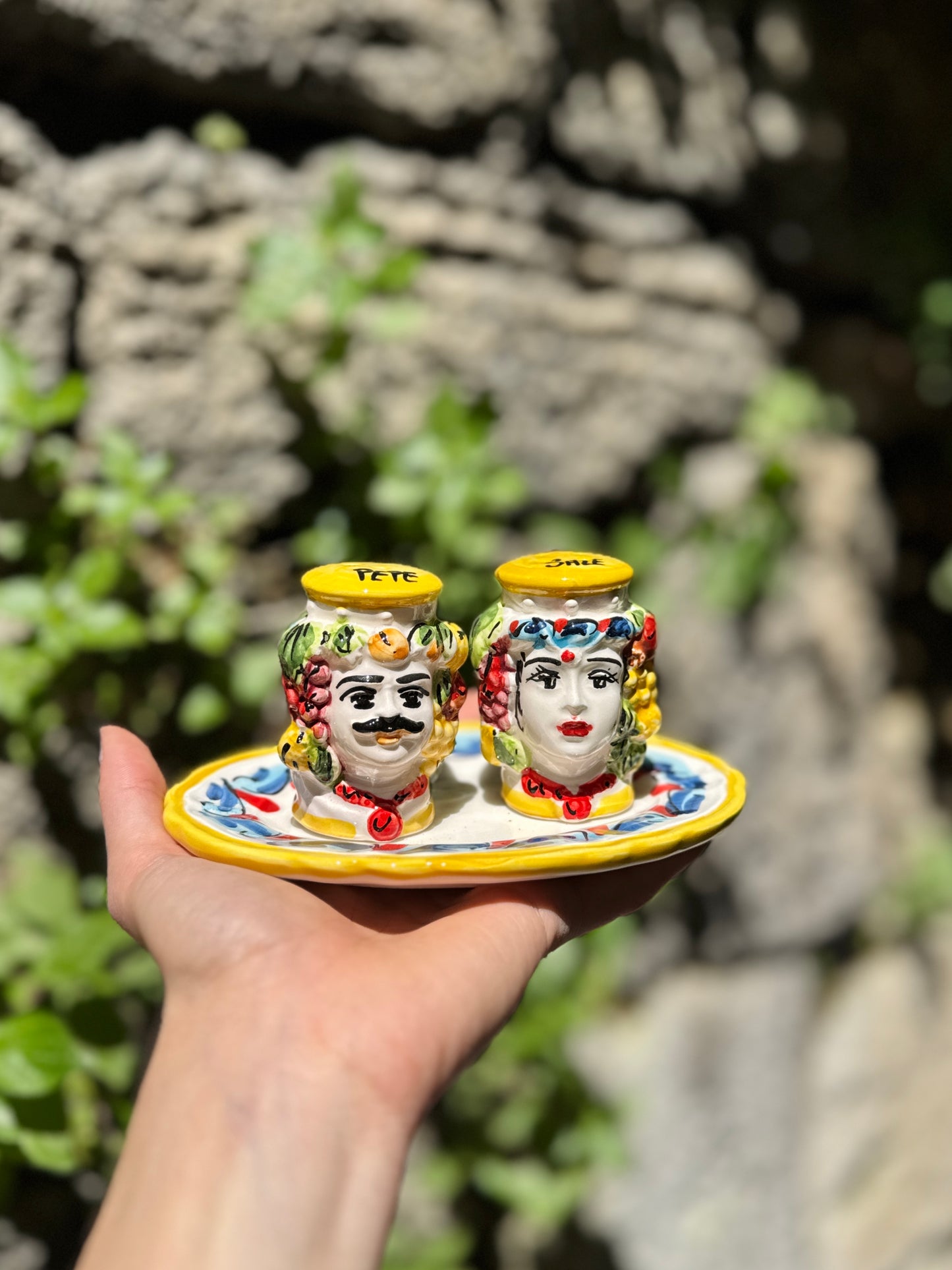 Colorful ceramic salt and pepper shakers on a plate held in front of a stone wall.