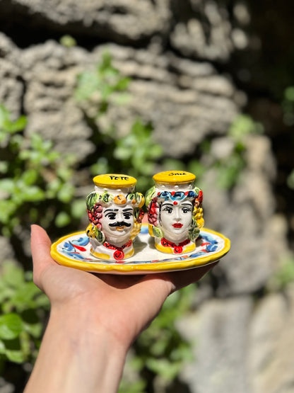 Colorful ceramic salt and pepper shakers on a plate held in front of a stone wall.
