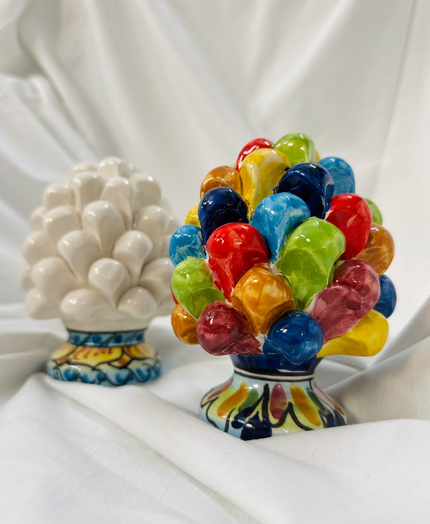 Two ceramic sculptures on a white fabric background, one multicolored and one white.
