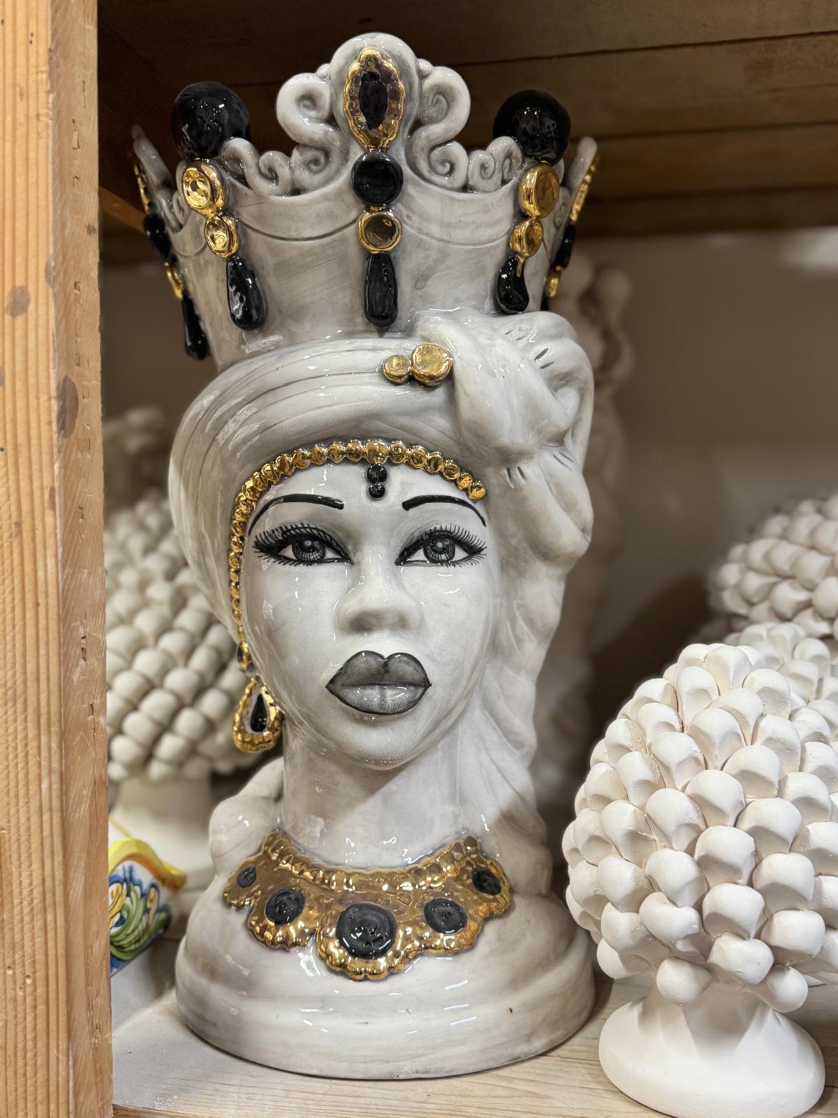 Handcrafted Sicilian Testa di Moro woman in ivory, black and gold displayed among traditional ceramic decorative objects.
