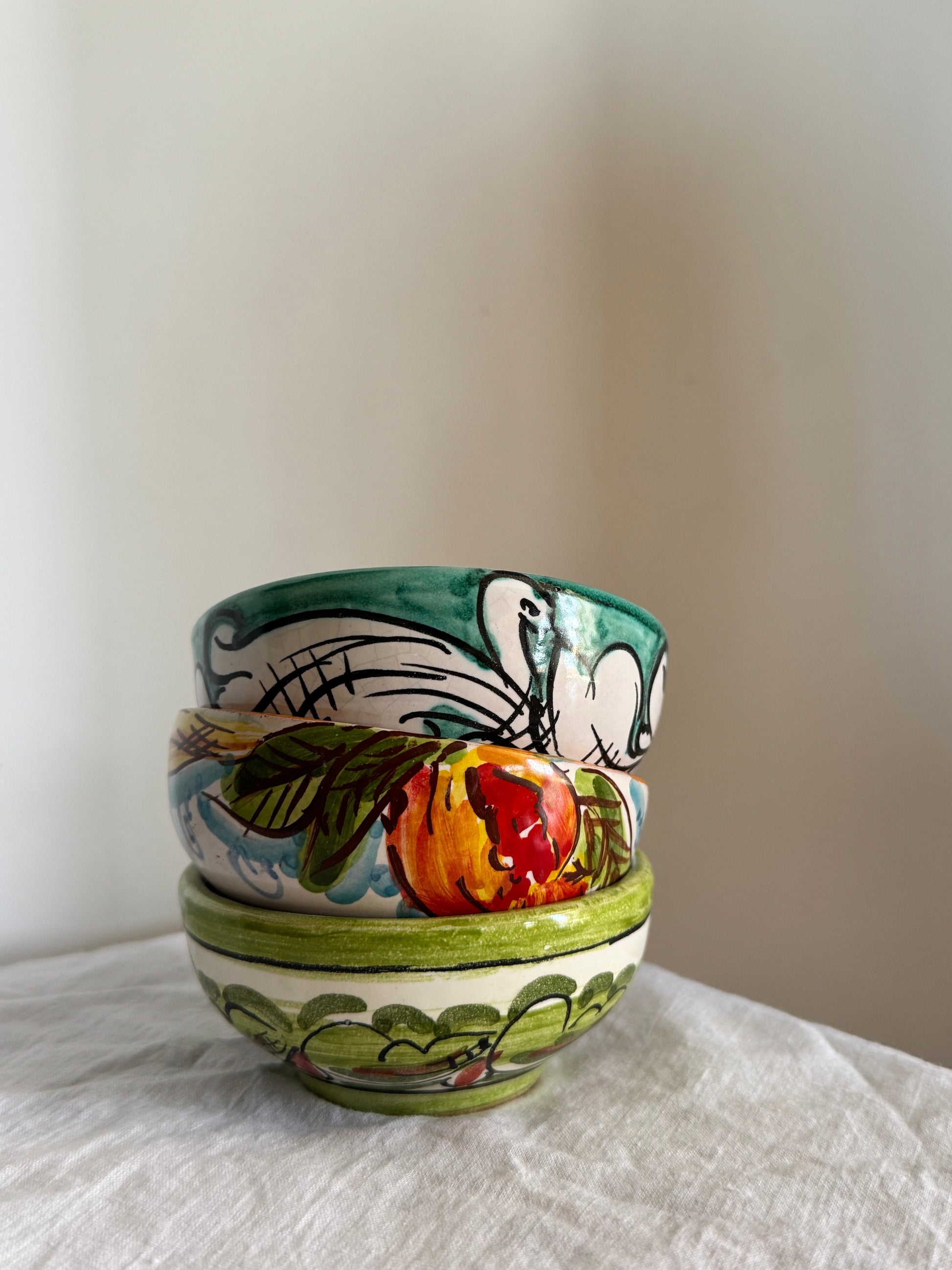 Set of three handcrafted Sicilian ceramic bowls with colorful Mediterranean, pomegranate and green majolica decorations, displayed together on natural linen.