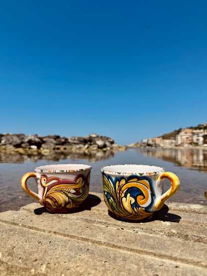 Handcrafted Sicilian ceramic cappuccino cups displayed by the sea, blending traditional majolica artistry with contemporary Mediterranean lifestyle.