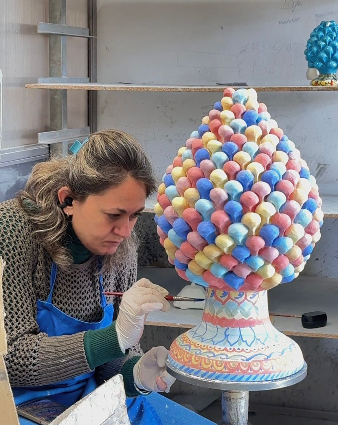 Female artisan hand painting a handcrafted Sicilian ceramic pine cone in a traditional Caltagirone pottery workshop.