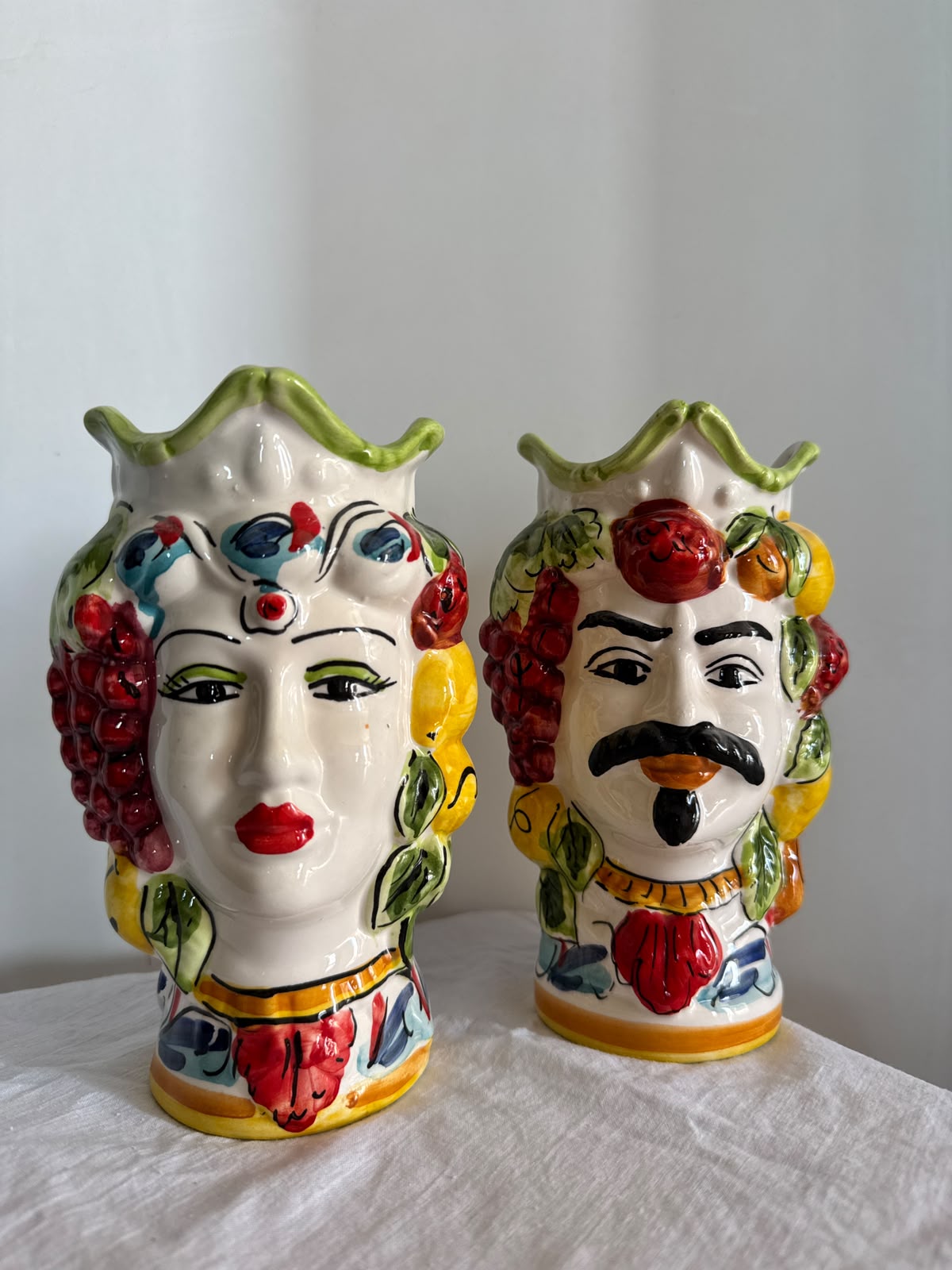 Handmade Sicilian Moor head ceramic vases displayed on natural white linen, featuring colorful fruit motifs and traditional Mediterranean decoration.