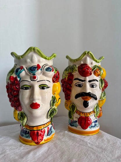 Handmade Sicilian Moor head ceramic vases displayed on natural white linen, featuring colorful fruit motifs and traditional Mediterranean decoration.