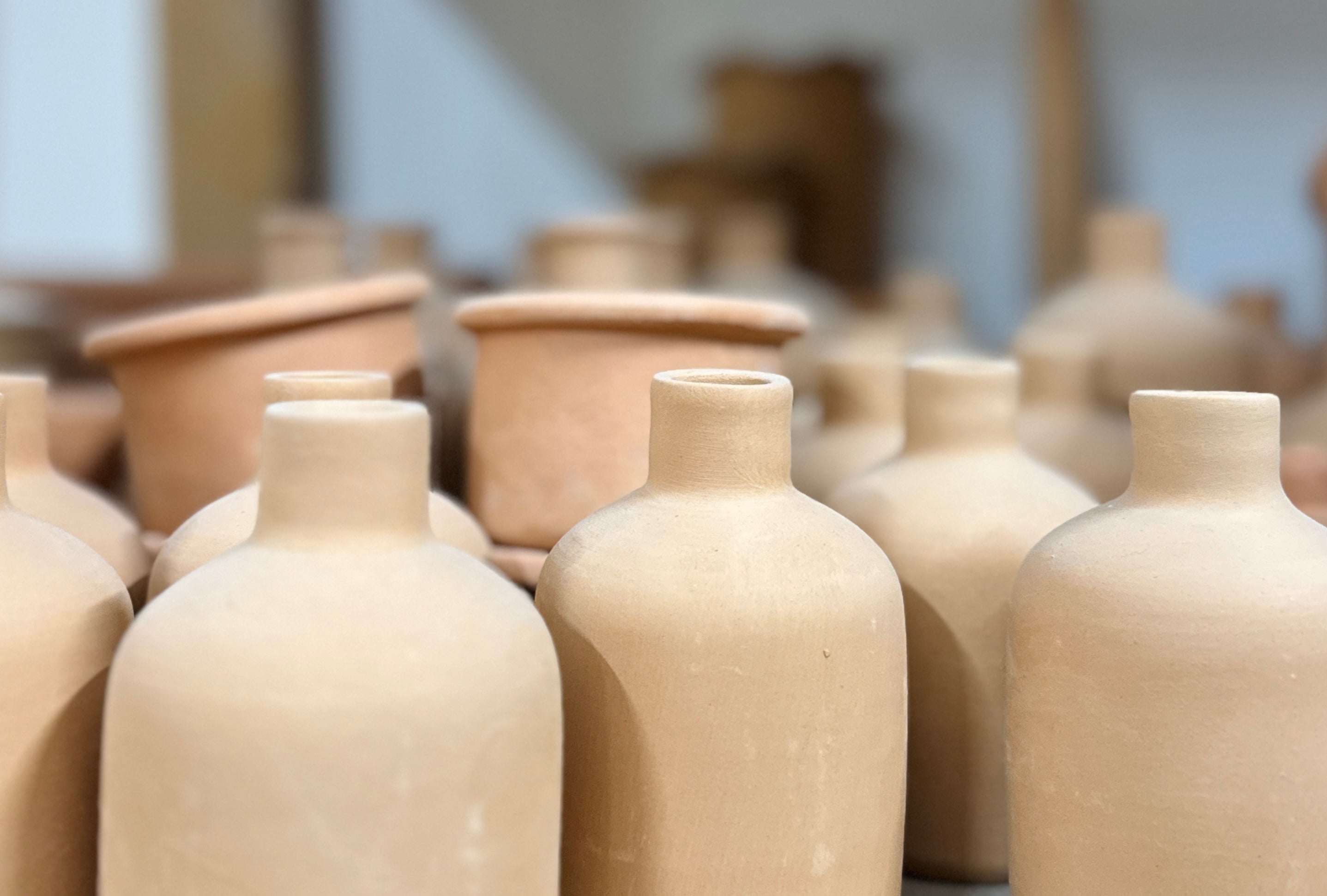Raw handmade Sicilian clay bottles and ceramic pieces inside a traditional artisan pottery workshop before glazing and decoration.