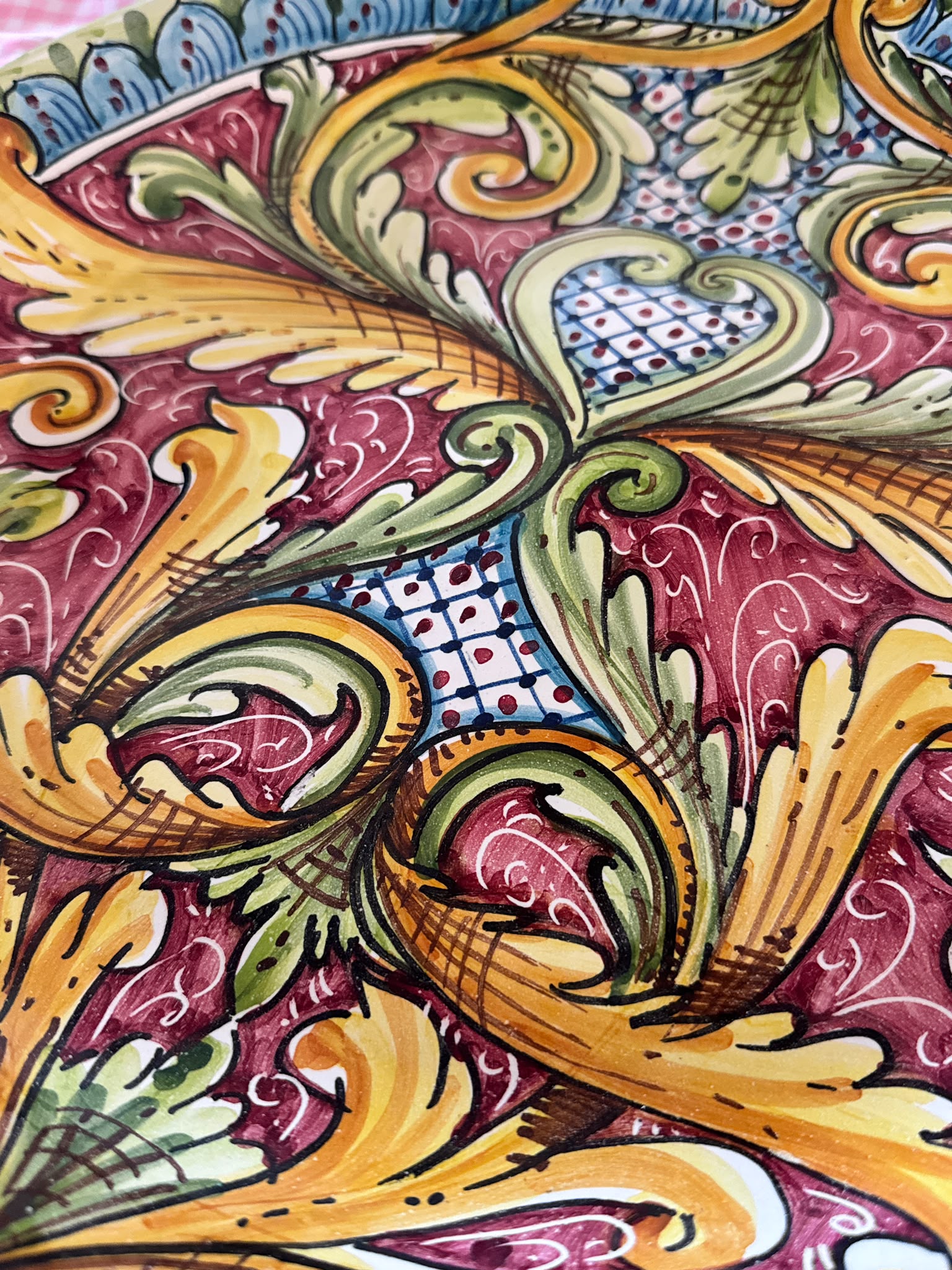 Close-up of a handcrafted Sicilian ceramic decorative plate with burgundy, yellow, green and blue baroque majolica motifs and glossy hand-painted details.