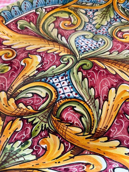 Close-up of a handcrafted Sicilian ceramic decorative plate with burgundy, yellow, green and blue baroque majolica motifs and glossy hand-painted details.