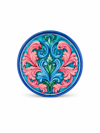 Handcrafted Sicilian ceramic decorative plate with symmetrical pink and blue majolica decoration on a clean white background.