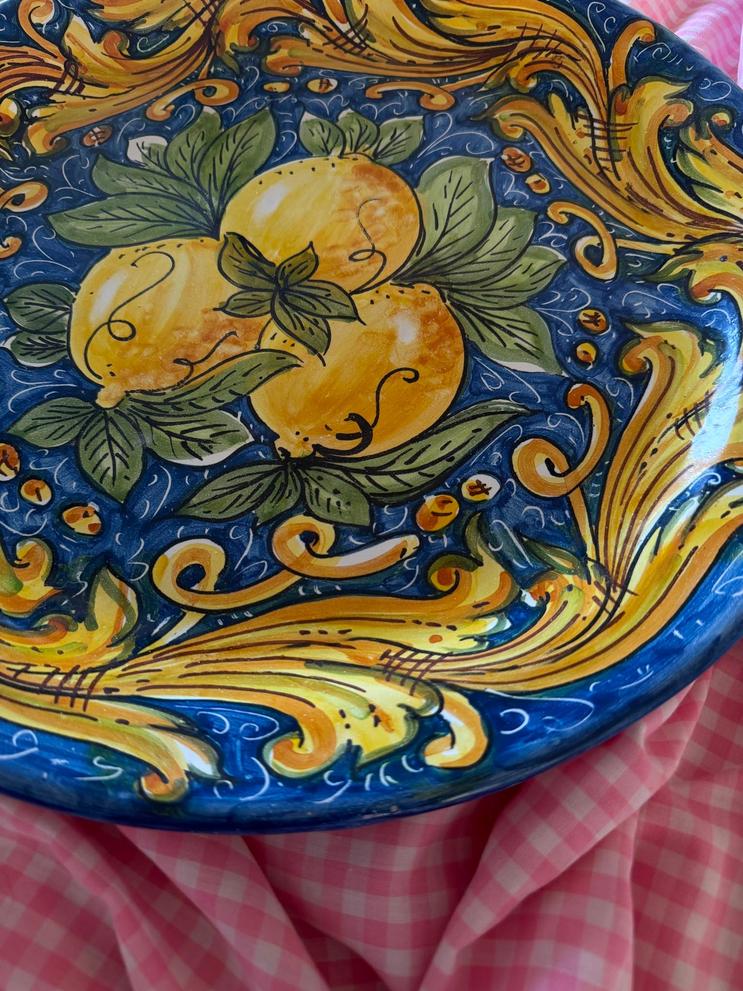 Close-up of a handcrafted Sicilian ceramic lemon plate with blue, yellow and green majolica decoration, showing glossy hand-painted artisan details.