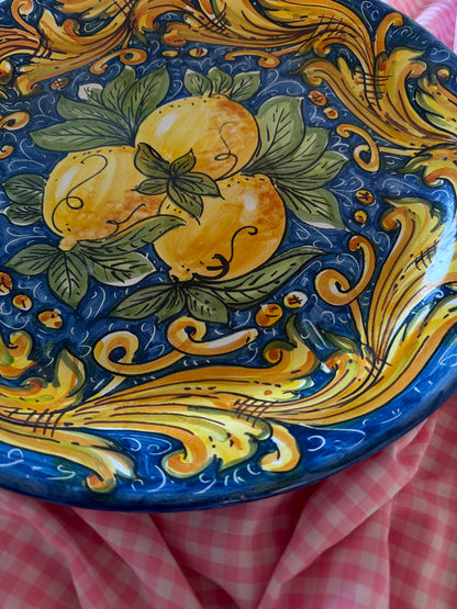 Close-up of a handcrafted Sicilian ceramic lemon plate with blue, yellow and green majolica decoration, showing glossy hand-painted artisan details.