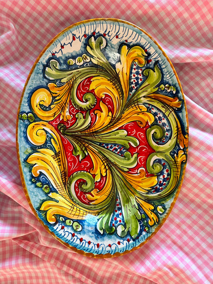 Close-up of a handcrafted Sicilian ceramic oval platter with colorful baroque majolica brushwork in red, yellow, green and blue tones.