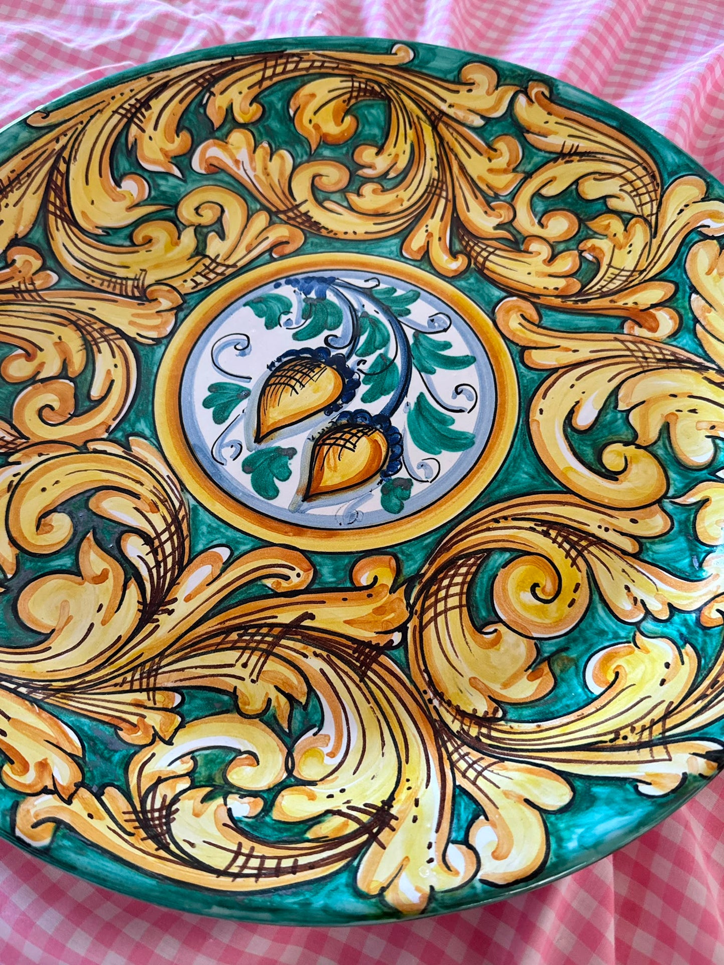 Close-up of a handcrafted Sicilian ceramic decorative plate with green and gold baroque majolica motifs, showing glossy hand-painted artisan details.