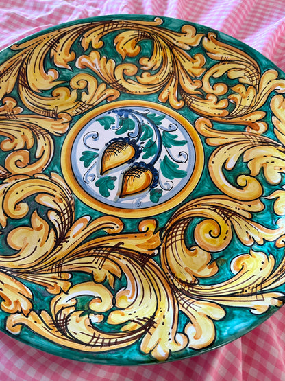 Close-up of a handcrafted Sicilian ceramic decorative plate with green and gold baroque majolica motifs, showing glossy hand-painted artisan details.