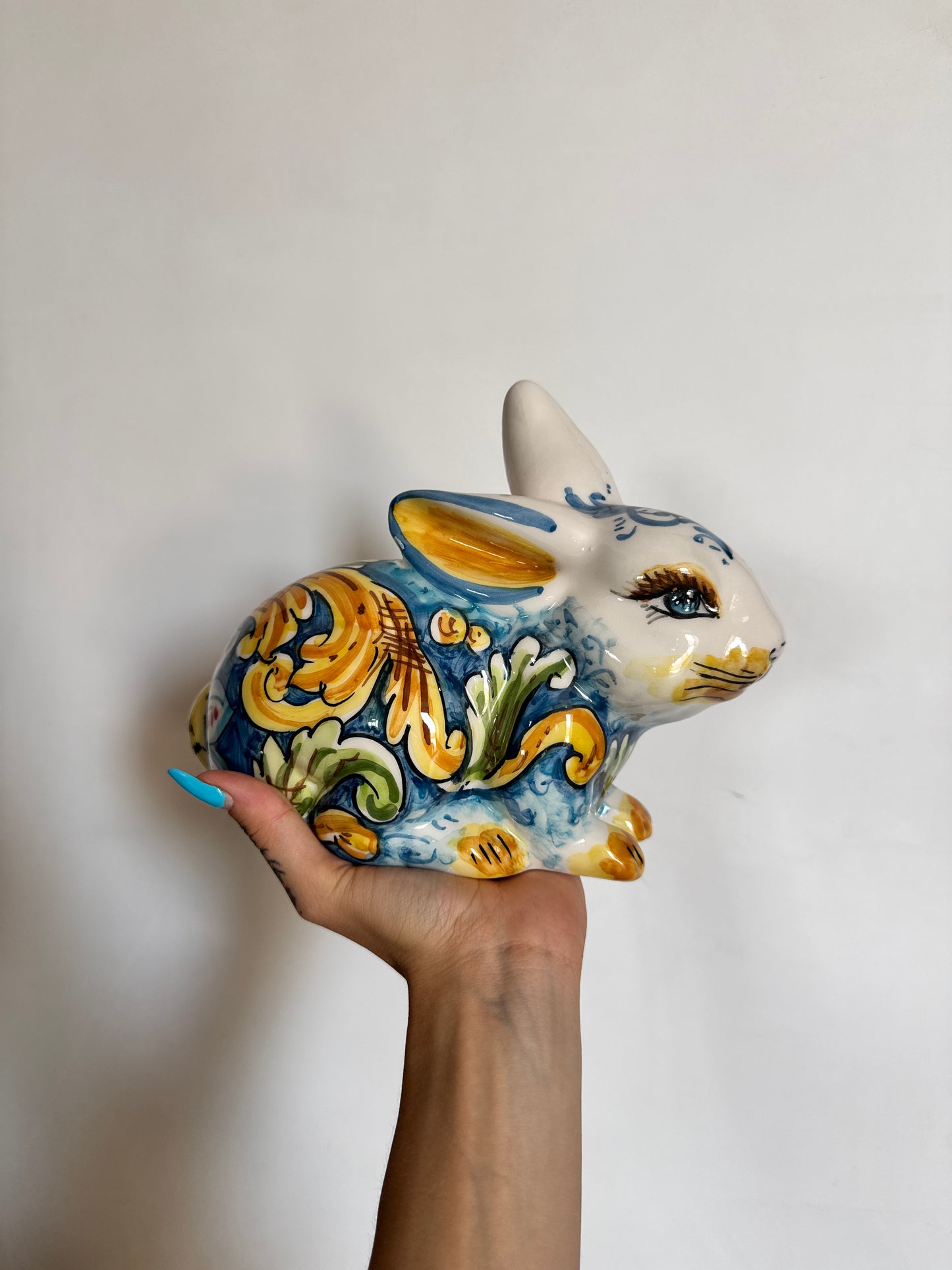 Handcrafted Sicilian ceramic rabbit sculpture with blue, yellow and green majolica decoration, displayed in hand to show scale and artisan details.