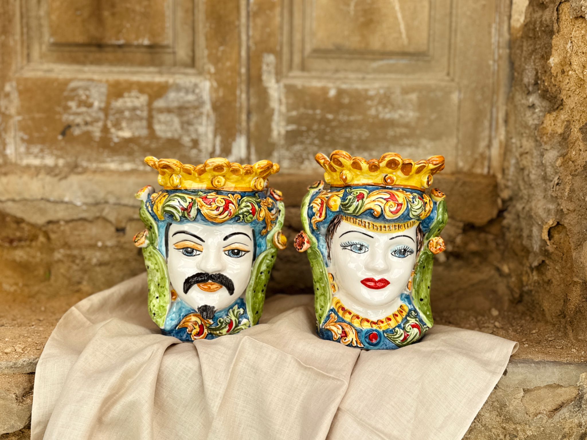 Handcrafted Sicilian Moor head ceramic vases from Caltagirone displayed in a rustic Mediterranean setting, featuring colorful traditional majolica details and royal crown design.