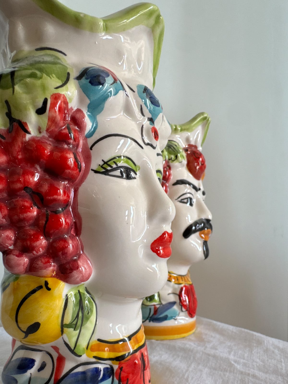 Close-up of handcrafted Sicilian Moor head ceramic vases showing glossy fruit decorations, painted facial details and traditional majolica colors.