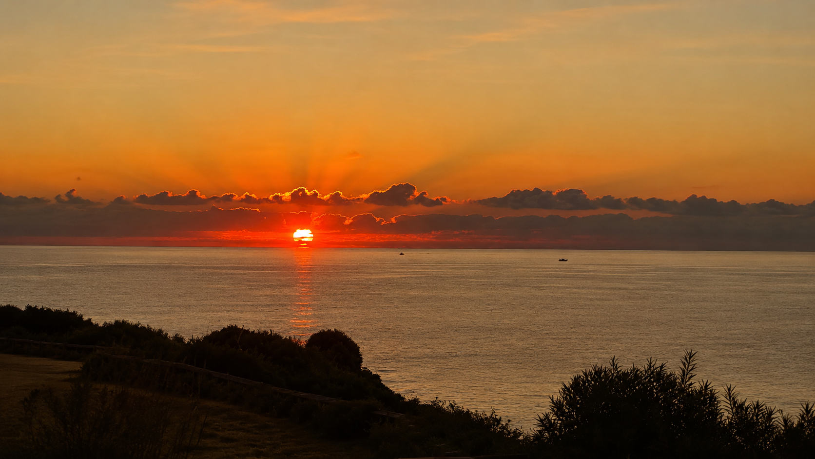 Golden sunrise over the Mediterranean Sea in Sicily with dramatic clouds and warm orange reflections on the water.