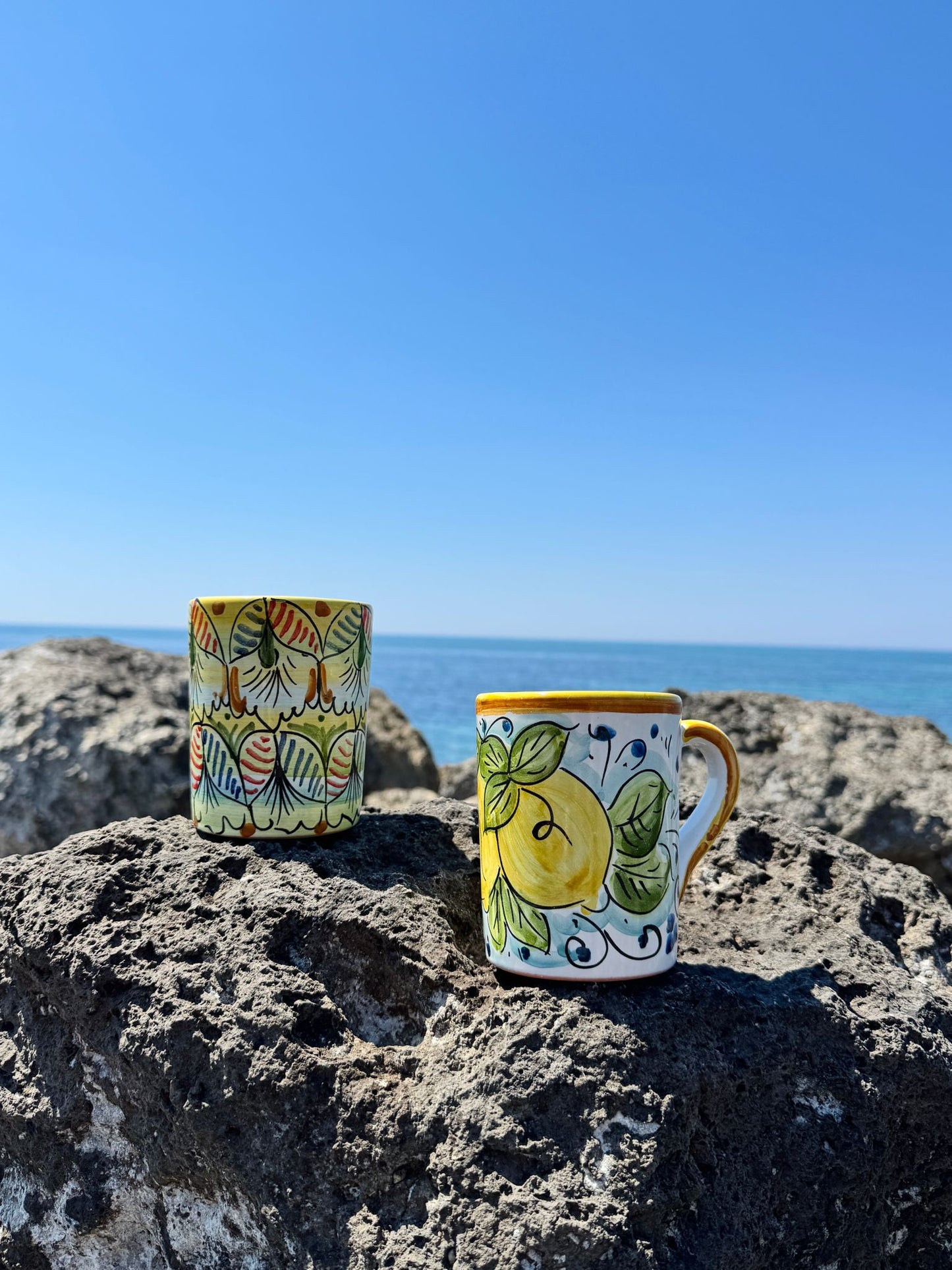 Artisan Sicilian ceramic drinkware collection photographed on the Mediterranean coast, celebrating traditional Italian craftsmanship and coastal living.